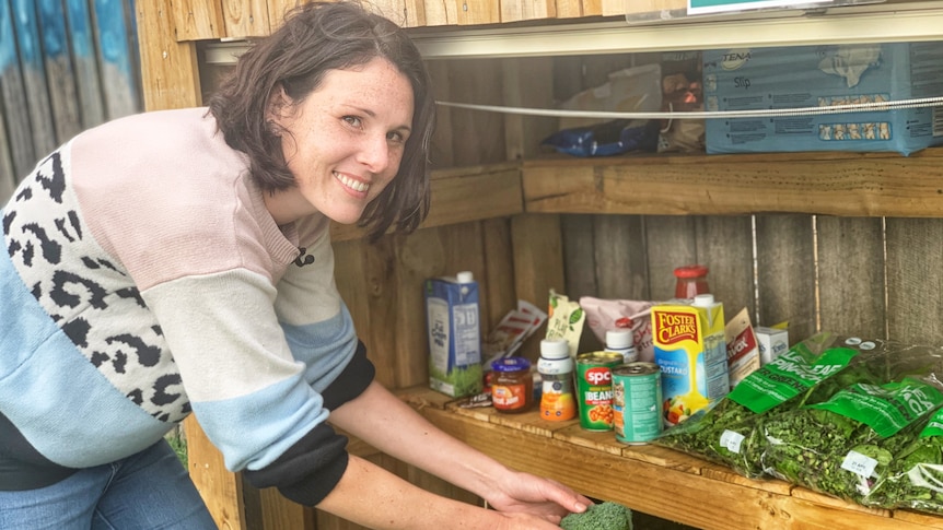 A woman smiles as she places broccoli on a shelf full of vegetables and pantry stores.