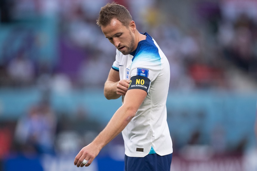 An England captain looks down as he touches an armband which has the message "No discrimination" on it.
