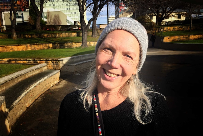 A woman wearing a grey beanie smiling with a green lawn and trees in background.