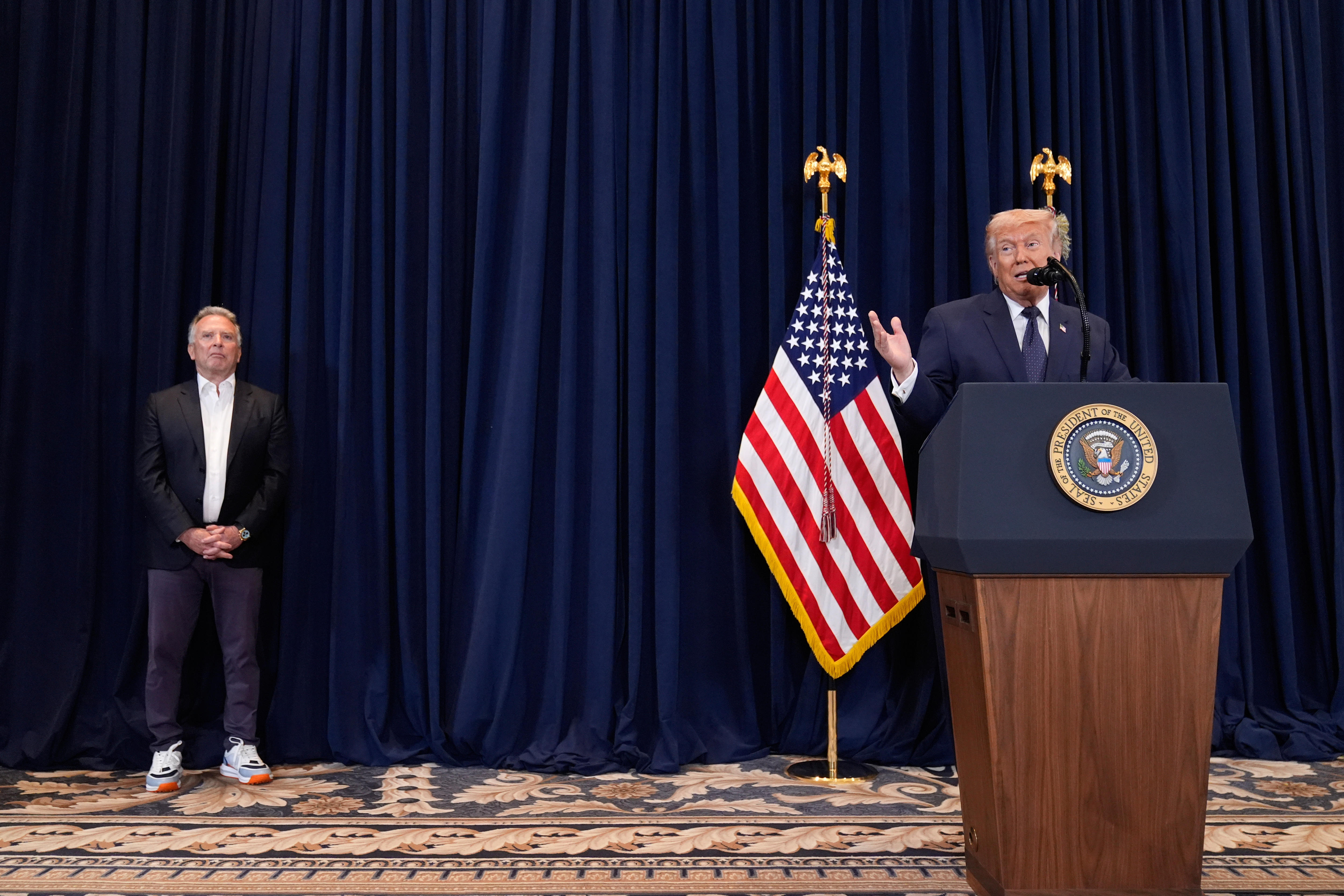 Trump waves his hand while speaking behind a podium on a stage