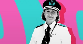 Black and white image of a smiling woman wearing pilot uniform, on brightly coloured pink and green background.