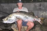 A man sitting on a rock with a huge fish across his lap.