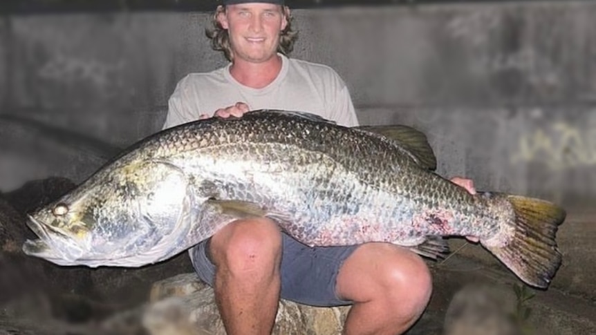 A man sitting on a rock with a huge fish across his lap.