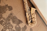 A saxophone on the floor covered in flood mud.
