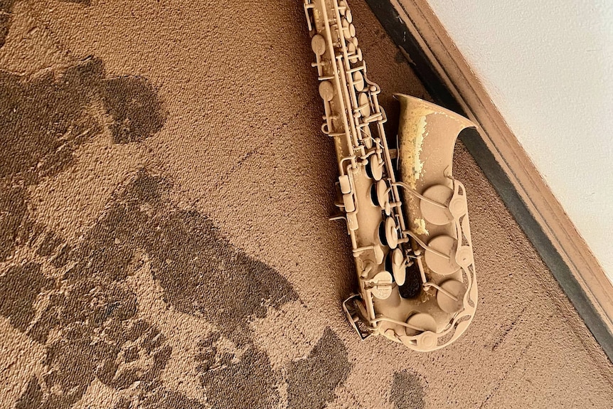 A saxophone on the floor covered in flood mud.
