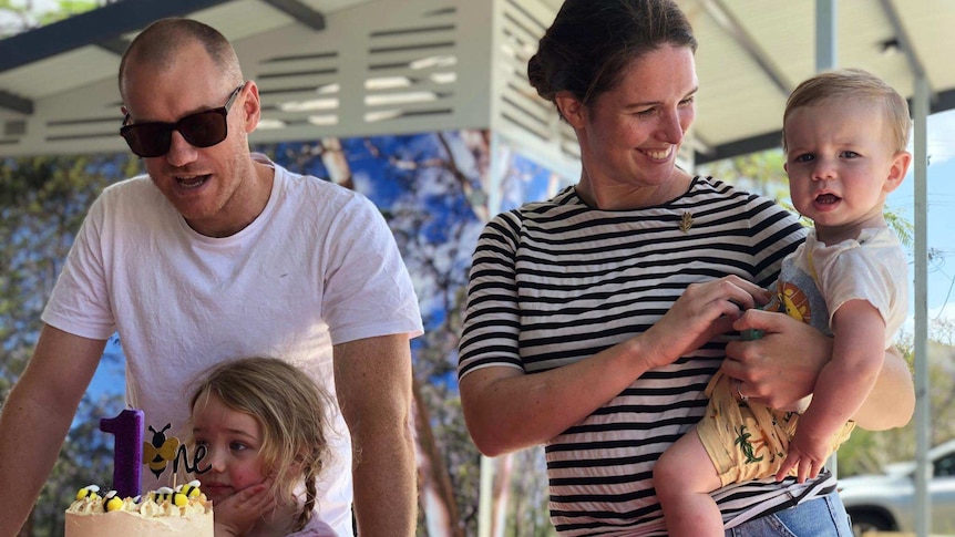 A family with two small kids gathered around a birthday cake.