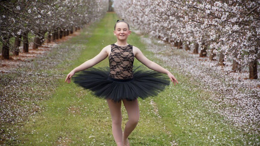 Jade Leedle in ballet costume among rows of trees in blossom.