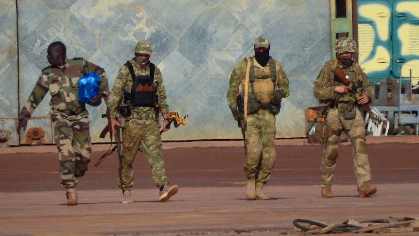 Four men in army fatigues walking with rifles.
