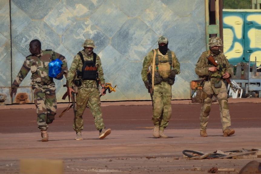 Four men in army fatigues walking with rifles.