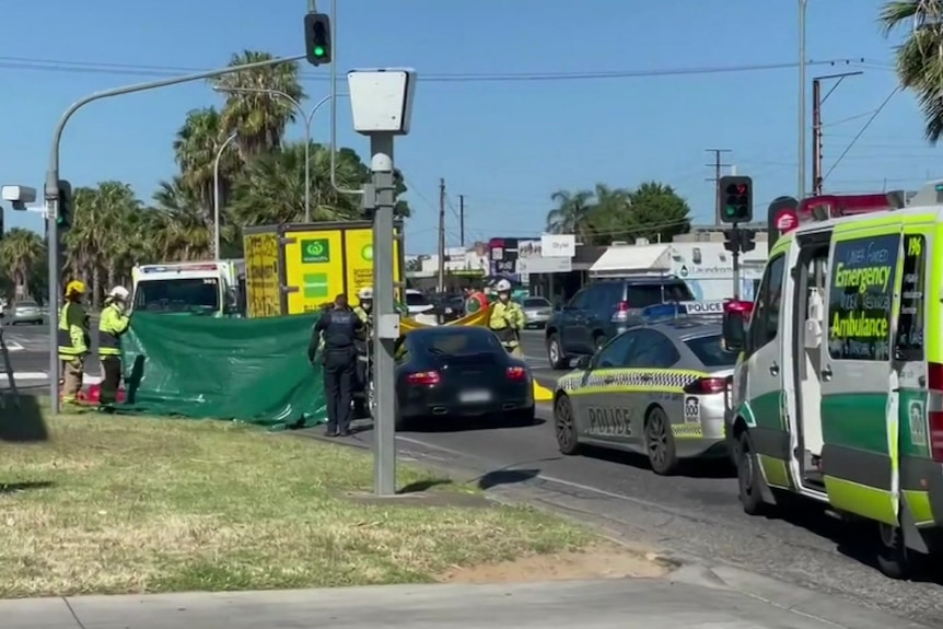 A black car between an OzHarvest truck and ambulances on a road