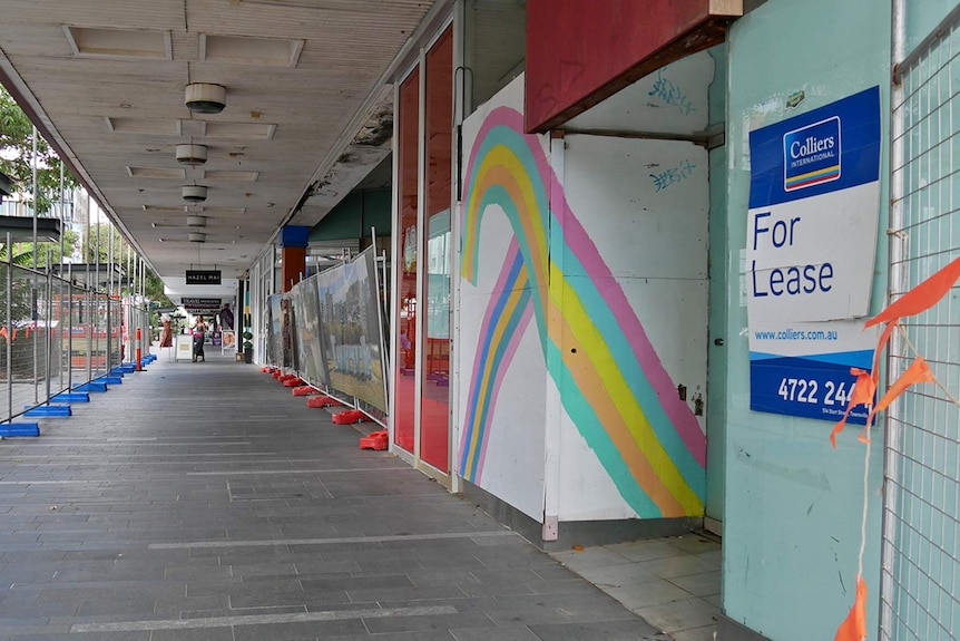 A series of empty shop fronts on Flinders Street in Townsville city, temporary fencing and For Lease signs are visible