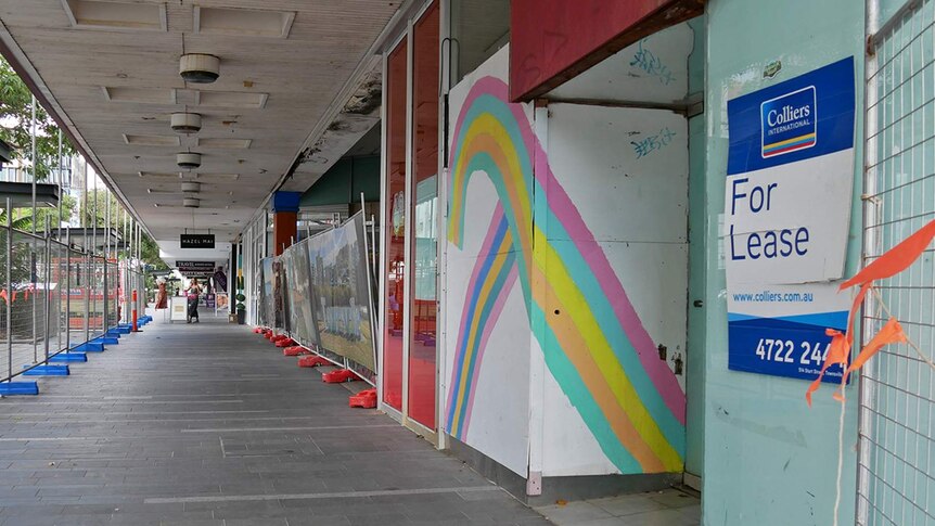 A series of empty shop fronts on Flinders Street in Townsville city, temporary fencing and For Lease signs are visible