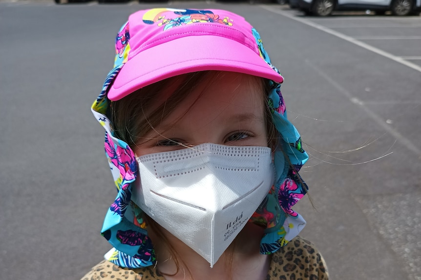 A young girl in a hat and a surgical mask