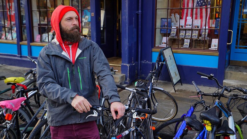 A man with long groomed facial hair adjusts his bike lock in oxford