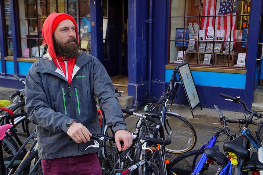A man with long groomed facial hair adjusts his bike lock in oxford