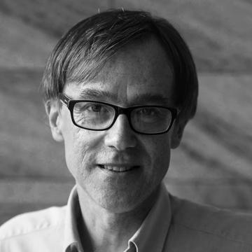 A black and white picture of a man with glasses looking into the camera.