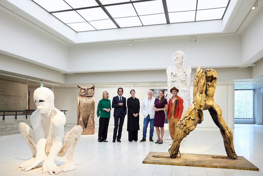 六个人站在一个艺术画廊里。 从左到右：女人、尼克·凯夫、女人、艺术家托马斯、另一个女人和布拉德·皮特。 