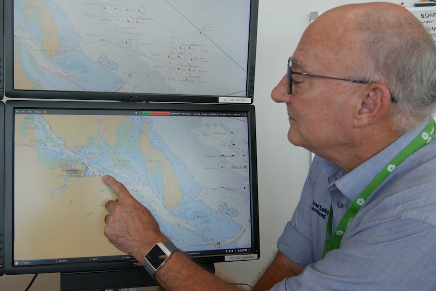 A man with grey hair and glasses pointing at a computer screen showing a map.