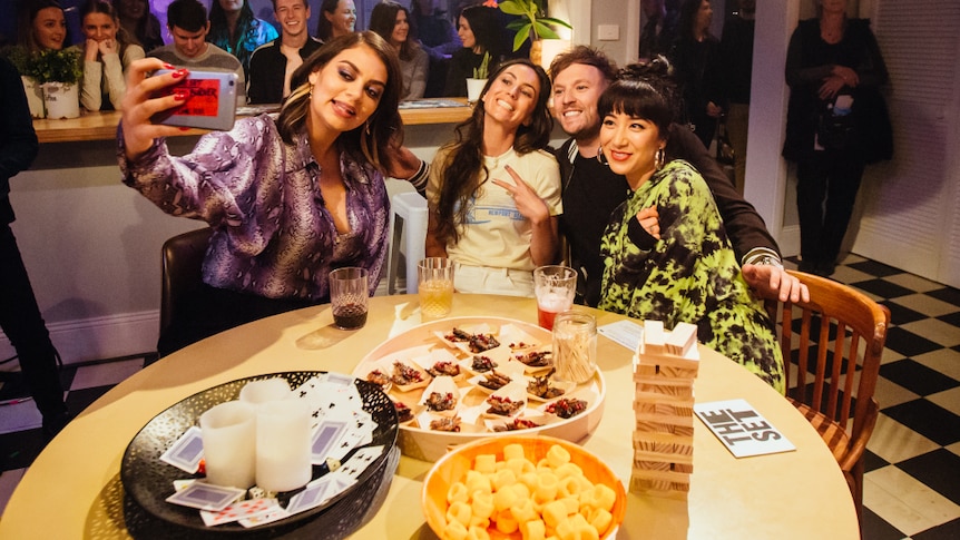 Image of Thelma Plum, Amy Shark, Dylan Alcott and Linda Marigliano taking a selfie at a kitchen table