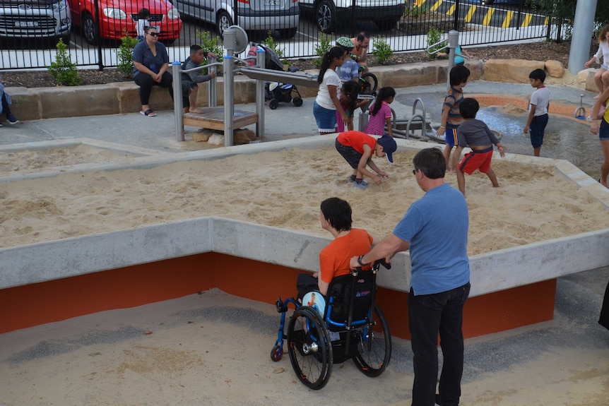 A boy in a wheelchair next to a raised sand pit at a playground