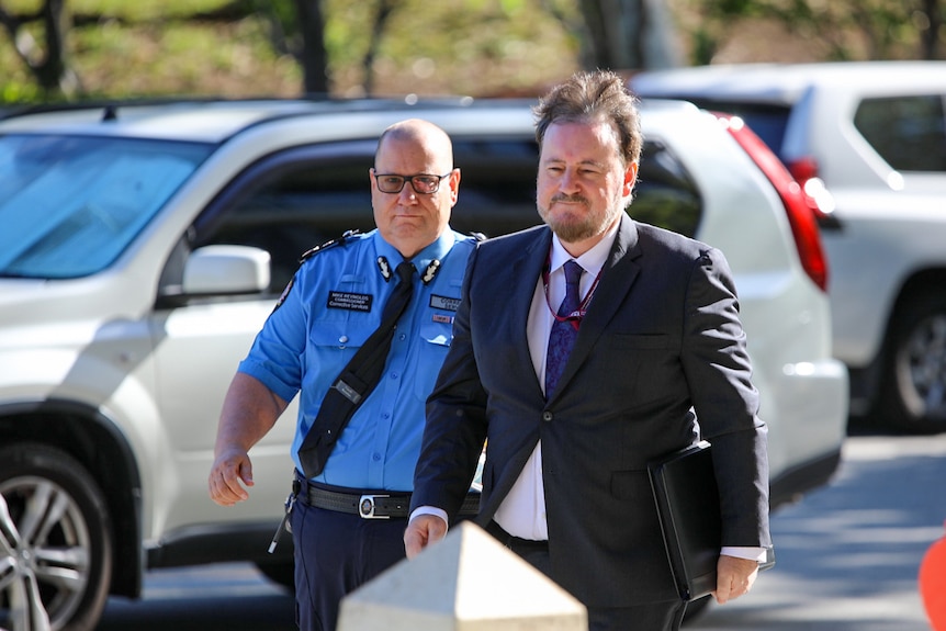 A man in a suit walks in front of an officer in a blue uniform.