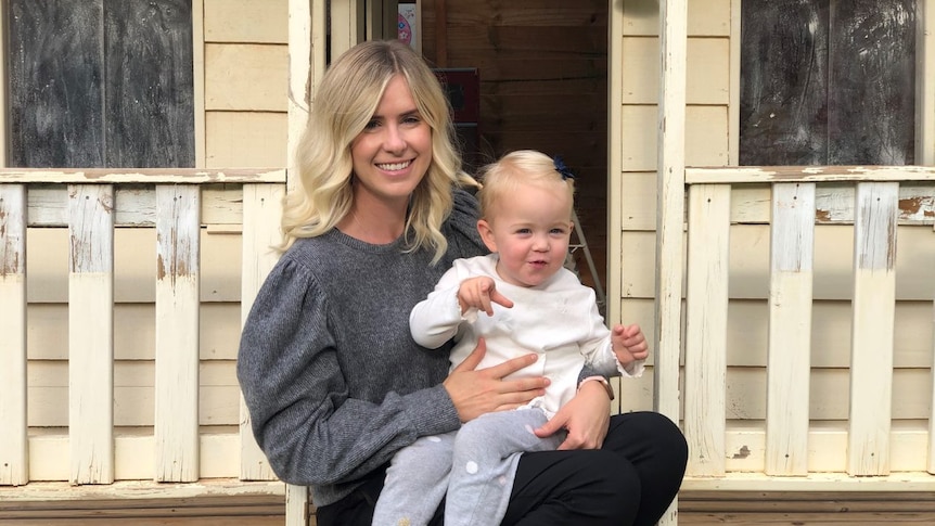 Alanna Wardle sits with her daughter on the step of a child's playhouse.