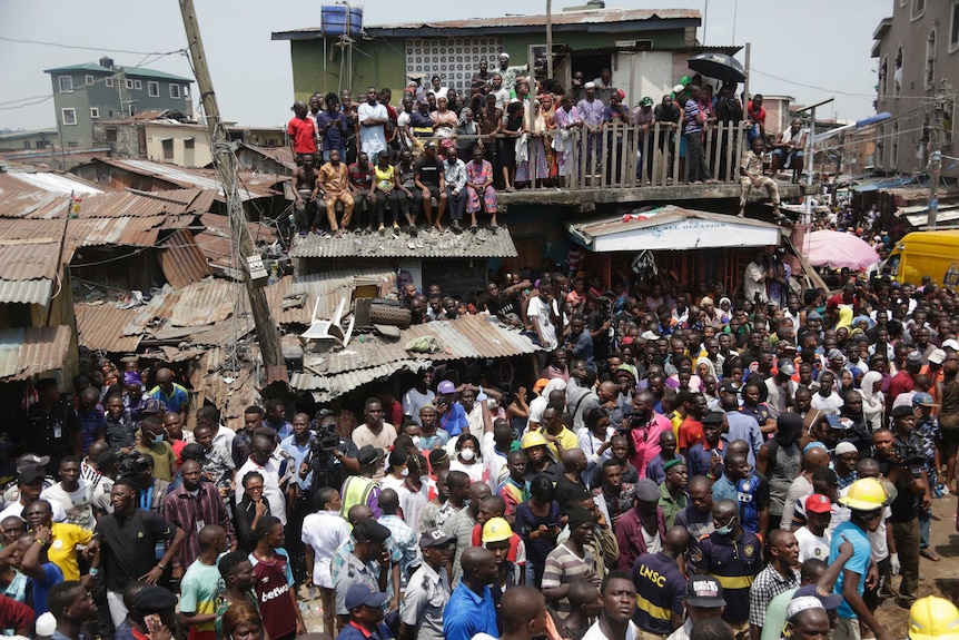 From a height, you can see a vast crowd of Lagos locals standing on a street and atop adjacent balconies opposite a rescue site.