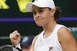 A female tennis player walks as she raises her right fist with a scoreboard in the background.