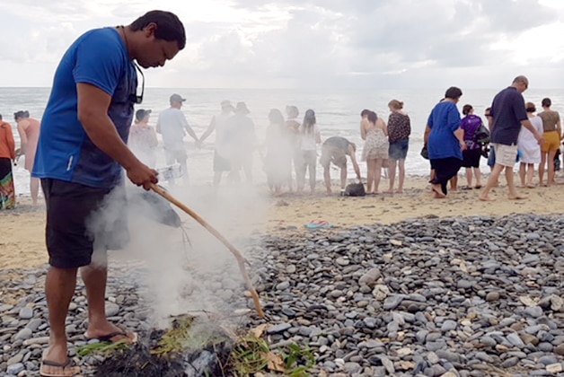Indigenous smoking ceremony out on Wangetti Beach, with line of people along beach facing the ocean.