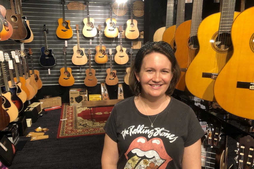 A young woman is surrounded by brand-new guitars hanging on the walls of a showroom.