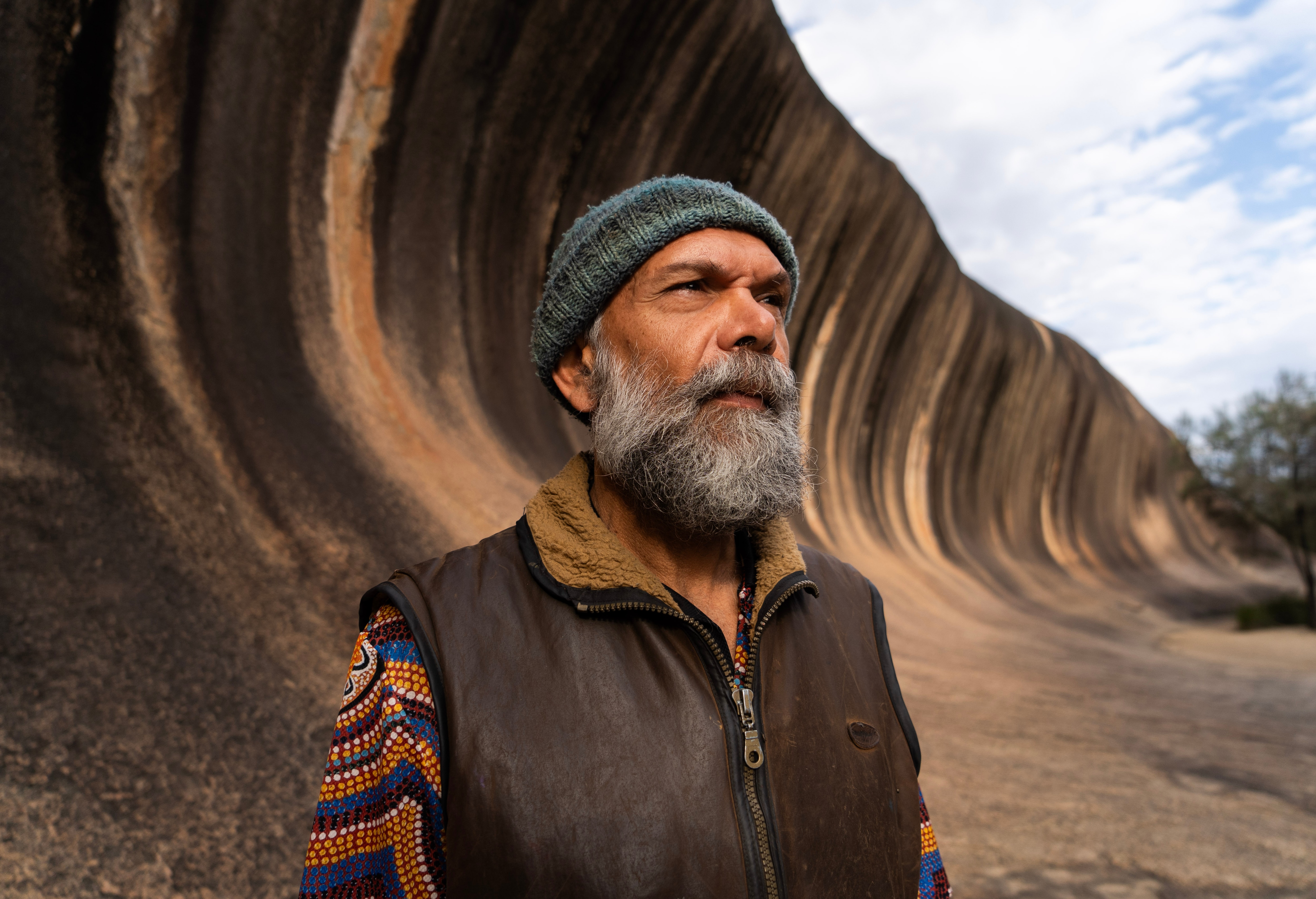 man with beard in front of giant rock wave