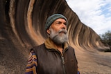 man with beard in front of giant rock wave