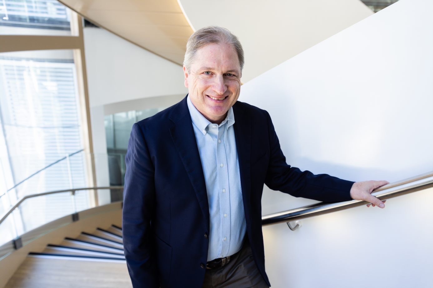 Man in suit holding stairs banisters facing the camera.