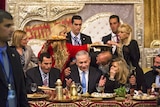 Benjamin Netanyahu seated at a table surrounded by people holding plates of food