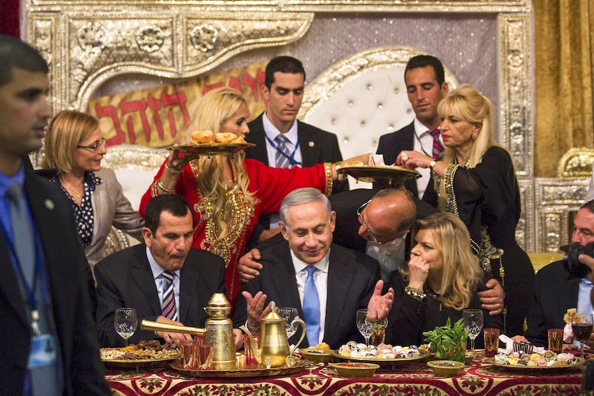 Benjamin Netanyahu seated at a table surrounded by people holding plates of food