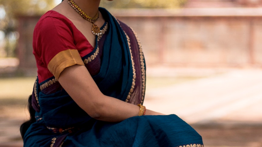 A woman wears a gold, red and navy saree and ornate necklace.