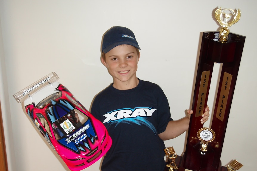 A boy holding a remote control car in one hand and a trophy in the other