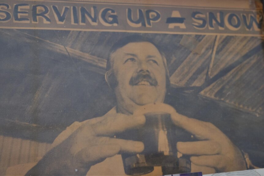 An old back and white photo of man holding onto three drinks with the caption 'serving up snow' 