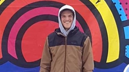 A young man in a hoodie standing in front of a painted rainbow.