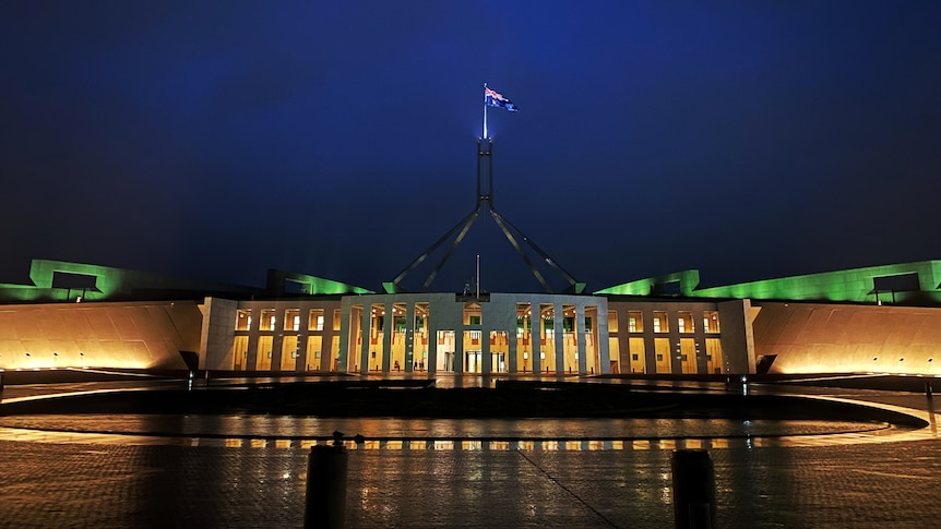 Pariament house from the front entrance at night with the flag lit up in the dark