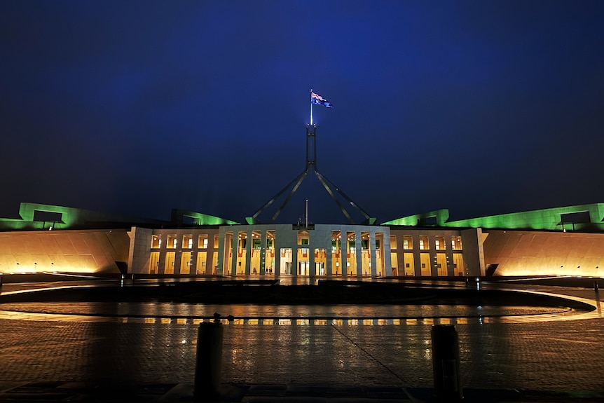 Pariament house from the front entrance at night with the flag lit up in the dark