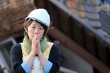 A woman reacts in front of a collapsed house