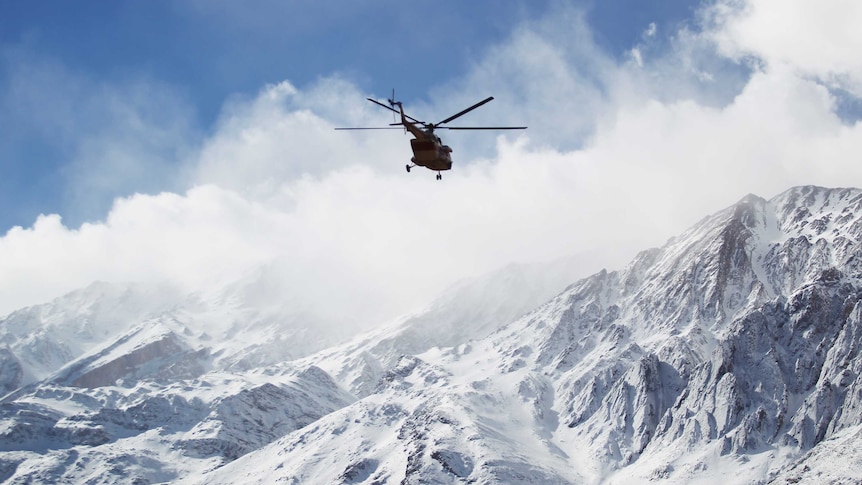 A rescue helicopter flies over the Dena mountains, which is covered in snow.