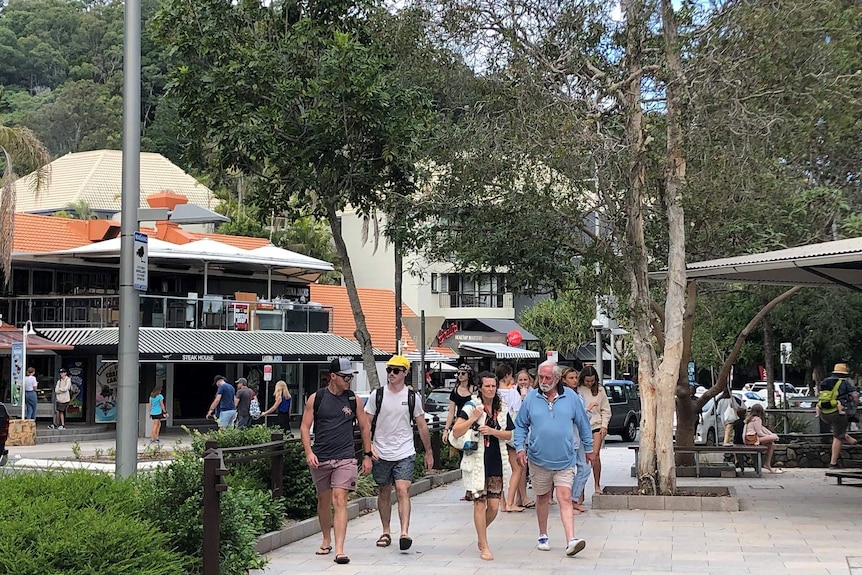 Groups of people walking past restaurants and cafes in a leafy street.