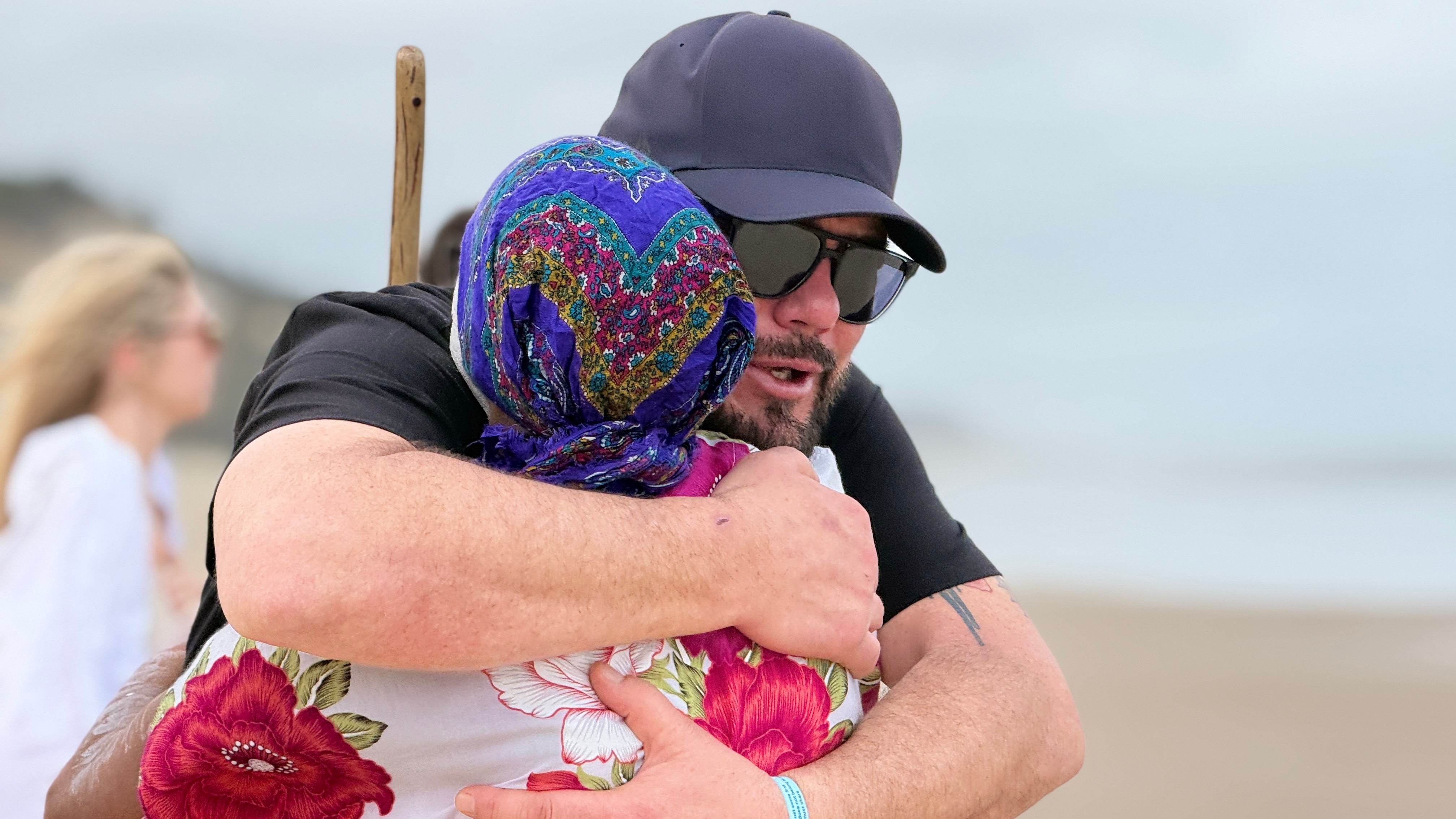 A man hugs a woman wearing a headscarf on the beach.