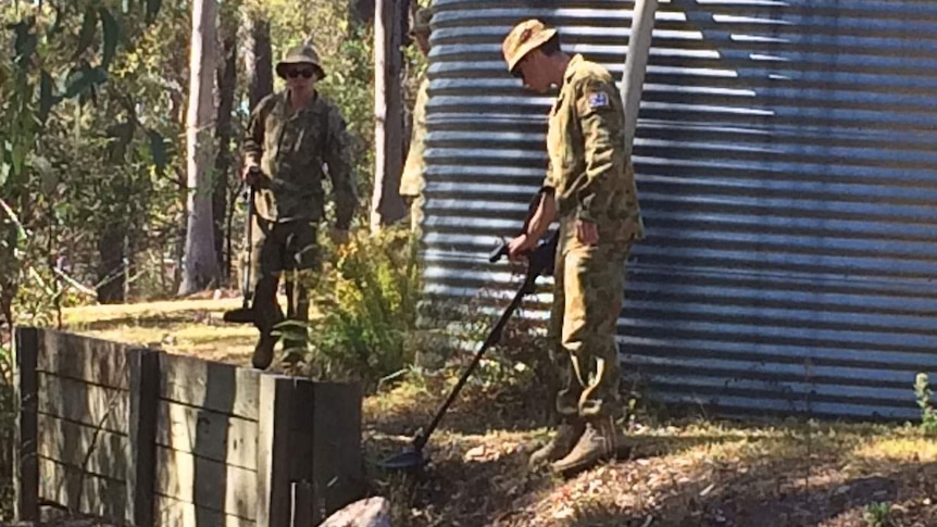 Australian soldiers search behind a water tank with metal detectors