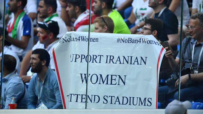 A supporter holds a large white sign saying 'Support Iranian women attend stadiums' in World Cup.