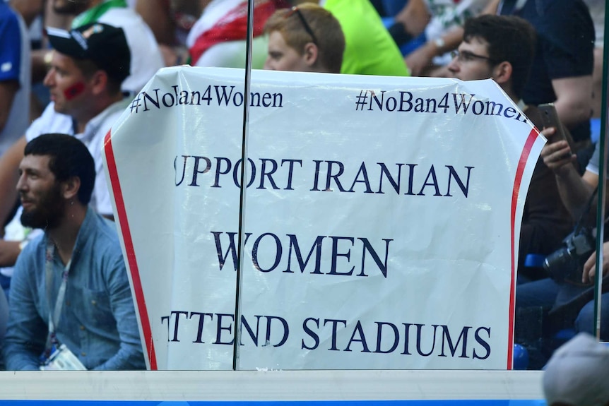 A supporter holds a large white sign saying 'Support Iranian women attend stadiums' in World Cup.