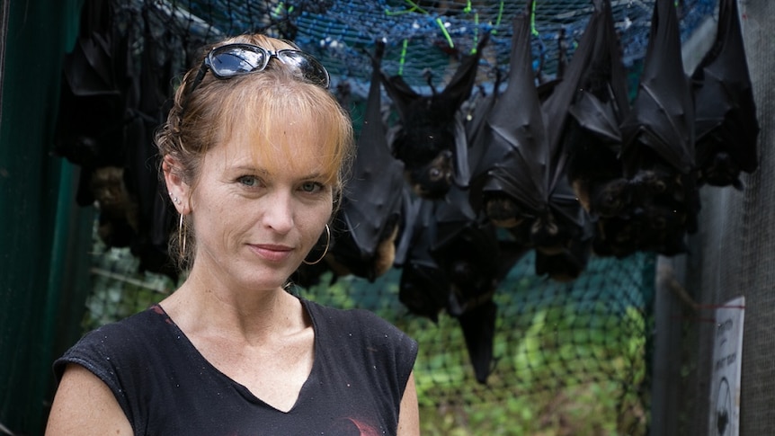 Woman stands in front of bats hanging from cage
