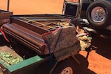 A photo of the piano wrapped in carpet and placed on the back of a trailer.